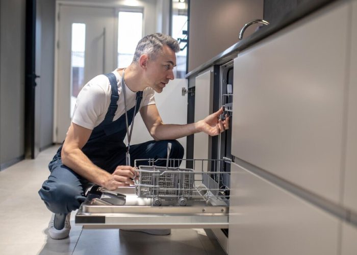 Man sitting near an open dishwasher and tools